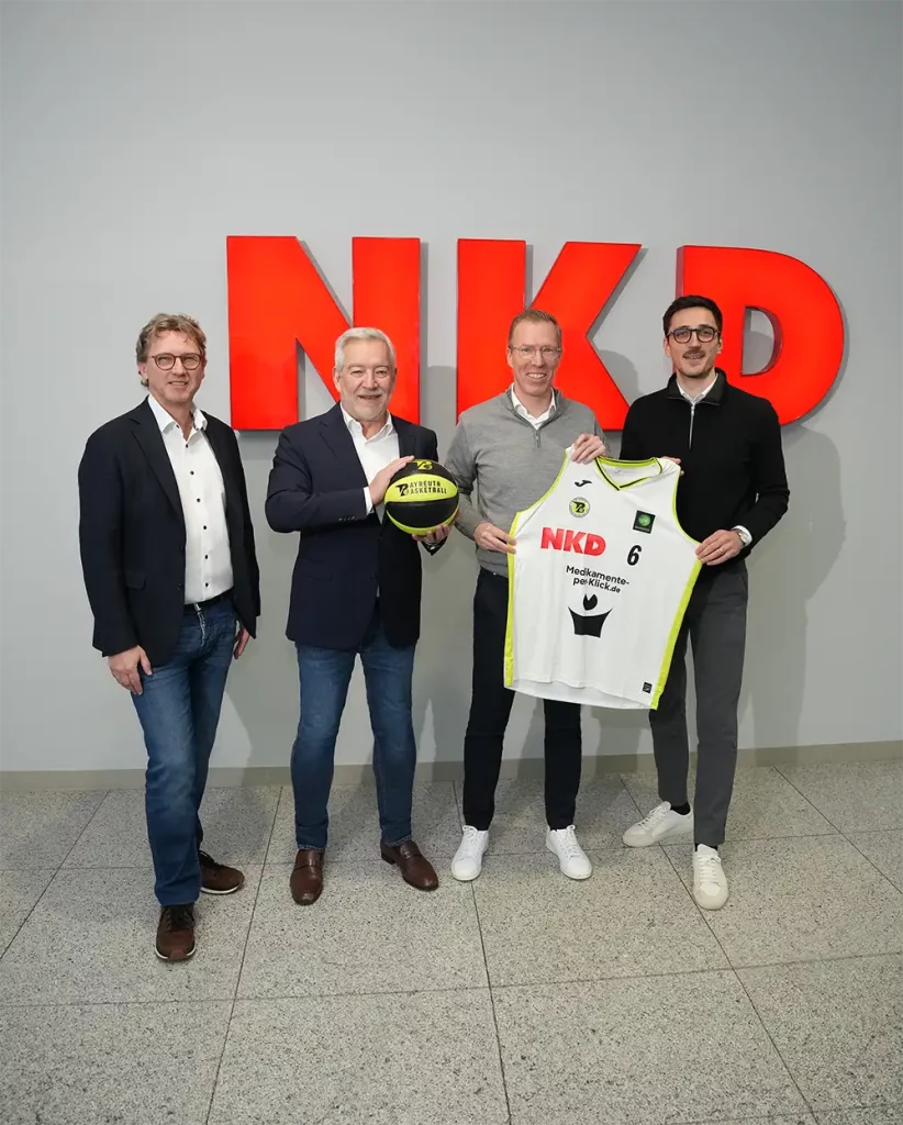 Zum Jahreswechsel verstärkt der Value Textile Discounter NKD sein regionales Engagement: Das Unternehmen mit Sitz in Bindlach ist ab sofort Premium-Sponsor des BBC Bayreuth, einem der traditionsreichsten Basketballvereine Deutschlands. Starke Partnerschaft für die Region Mit der Premium-Partnerschaft unterstreicht NKD seine enge Verbundenheit mit der Region Oberfranken. Der BBC Bayreuth, der in der 2. Basketball Bundesliga spielt und auf eine über 60-jährige Vereinsgeschichte zurückblickt, erhält damit einen starken Partner aus der unmittelbaren Nachbarschaft. NKD wird ab dem Rückrundenstart auf der Trikotvorderseite des Basketball-Bundesligisten aufmerksamkeitsstark präsent sein. Nils Bolender, CFO der NKD-Firmengruppe, erklärt: „Als Unternehmen mit Hauptsitz in Bindlach fühlen wir uns der Region Oberfranken besonders verbunden. Der BBC Bayreuth steht für Tradition, Leidenschaft und Teamgeist – Werte, die auch uns bei NKD wichtig sind. Mit unserem Engagement möchten wir den Basketballsport in unserer Heimatregion stärken und gemeinsam mit dem BBC Bayreuth die Begeisterung für den Sport in der Region weiter fördern.“