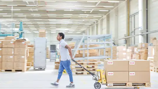 Ein Mitarbeitende zieht einen Wagen durch die Logistik